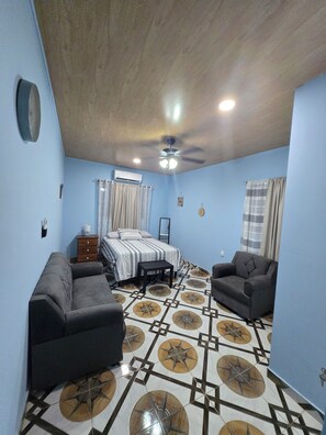 A bedroom with a bed, two sofas, a small table, and a ceiling fan.
