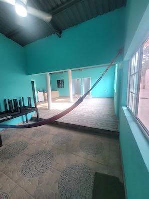 Una habitació amb parets color turquesa, un terra amb dibuixos, un hamaca i una finestra.