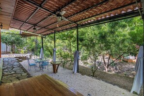 Un espace extérieur aménagé en patio, doté d’un coin salon couvert, d’un chemin en pierre et entouré de verdure.