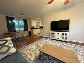 A living room with a sofa, a coffee table, a TV, and a kitchen in the background.