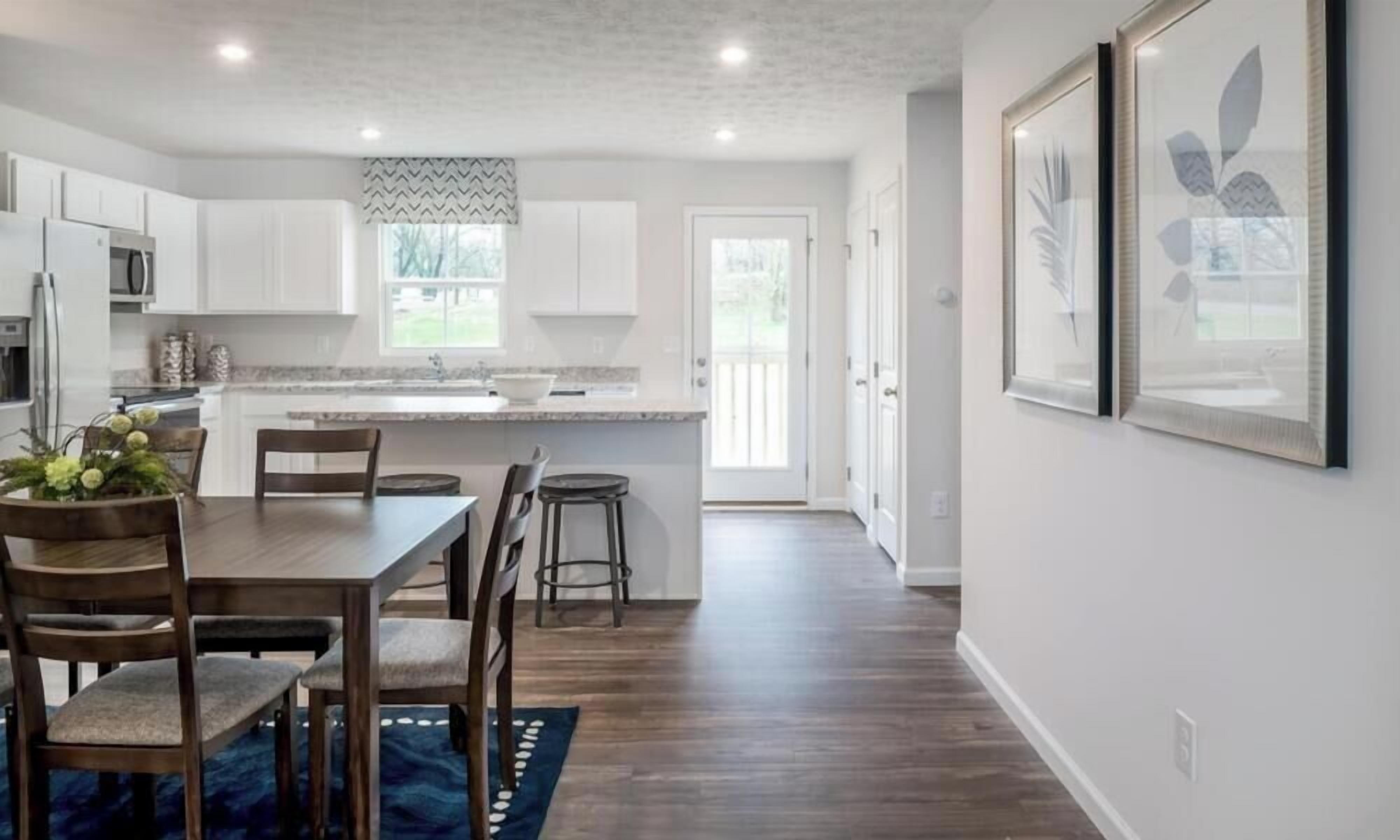 Une cuisine moderne avec des meubles blancs, une table à manger en bois et un tapis bleu.