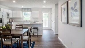 Een moderne keuken met witte kastjes, een houten eettafel en een blauw vloerkleed.