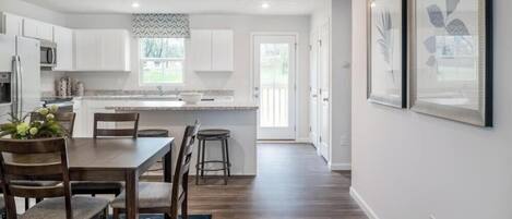 A modern kitchen with white cabinets, a wooden dining table, and a blue rug.