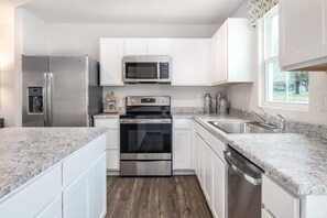 A kitchen with white cabinets, stainless steel appliances, granite countertops, and a window providing natural light. - Newly built 4-bedroom home with mountain views in charming Bedford community. (Bedford)