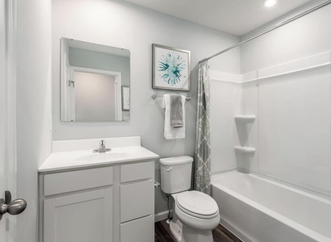 A bathroom with a white sink, toilet, and bathtub. There is a towel rack with a towel hanging on it, and a framed picture on the wall.