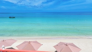 Ein Strand mit klarem türkisblauem Wasser, ein Boot in der Ferne und Sonnenschirme im Sand.