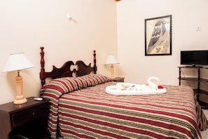 Ein Hotelzimmer mit einem hölzernen Bett, gestreifter Bettwäsche, zwei Nachttischlampen, einem Flachbildfernseher und einem gerahmten Kunstwerk an der Wand.
