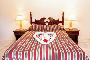 Una cama con una toalla dispuesta en forma de corazón, ropa de cama a rayas y dos lámparas de noche.