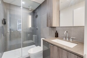 Ein modernes Badezimmer mit Duschkabine aus Glas, einer weißen Toilette und einem beige farbenen Waschtisch mit Waschbecken und Spiegel.