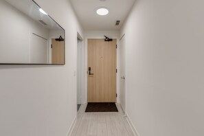 A narrow hallway with a wooden door at the end, a mirror on the left wall, and a light fixture on the ceiling. - Luxe Nobu | 2BR + Private 750 SqFt Terrace in the Heart of Toronto (Toronto)