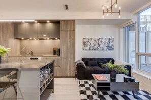Eine moderne Küche mit einer zentralen Kochinsel, einem dunkelgrauen Sofa und einem großen Fenster mit Blick auf die Stadt.