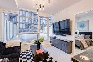 Una sala de estar moderna con un sofá, una mesa de centro, televisor y un amplio ventanal con vista a la ciudad.