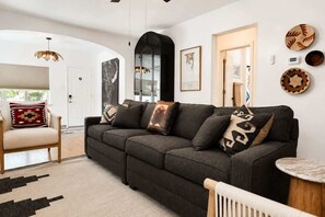 A modern living room with a dark grey sofa, a wooden chair, and a round side table. - Old Town Buffalo+Private Hot Tub+Near Old Town+Pet Friendly! (Albuquerque)
