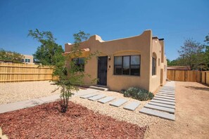 Une maison de plain-pied avec un toit plat, un porche à l’avant et un petit arbre dans le jardin.