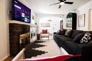 Un salon avec une cheminée, un canapé, un téléviseur fixé au mur et un ventilateur de plafond.