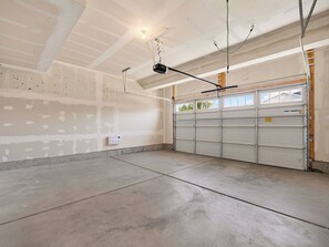 Eine Garage mit Betonboden, einer weißen Garagentür und einer Decke mit freiliegenden Balken und Verkabelung.