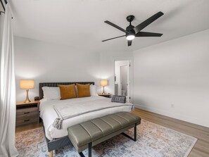 Ein Schlafzimmer mit einem Bett, Nachttischlampen, einer Bank, einem Deckenventilator und einem gemusterten Teppich.