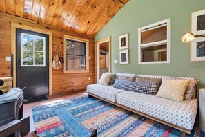 Ein gemütliches Zimmer mit Holztür, einer Couch mit gemusterten Kissen, einem Teppich und gerahmten Bildern an der Wand.