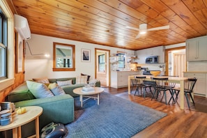 A cozy interior with a wooden ceiling, a dining area, a kitchen, and a living room with a sofa and coffee table. - Cozy 3BR Bethel retreat with sauna, fireplace, Wi‑Fi, and deck. (Bethel)