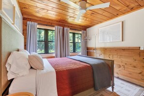 A wooden-paneled room with a bed, a ceiling fan, and a window with curtains. - Cozy 3BR Bethel retreat with sauna, fireplace, Wi‑Fi, and deck. (Bethel)