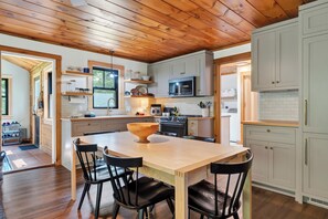A modern kitchen with wooden cabinets, a central island with chairs, and a microwave above the stove. - Cozy 3BR Bethel retreat with sauna, fireplace, Wi‑Fi, and deck. (Bethel)