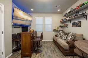 Una sala de estar con zona de bar, un televisor montado en la pared y una colección de maquetas de vehículos en estantes.