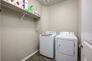 Un cuarto de lavandería con dos lavadoras, un estante con productos de limpieza y una puerta.
