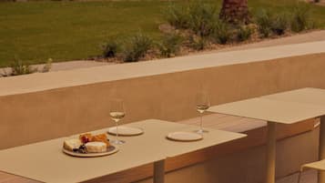 Un espacio de comedor al aire libre con una mesa larga y cuatro sillas, rodeado por un jardín con plantas y un muro de ladrillo.