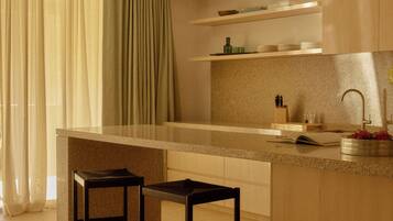A modern kitchen with a central island, two bar stools, a built-in sink, and a window with curtains.