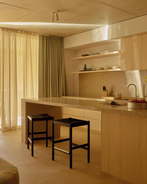 A modern kitchen with a central island, two bar stools, a built-in sink, and a window with curtains.