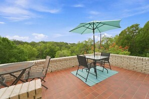 Eine Terrasse im Freien mit Tisch, Stühlen, einem grünen Sonnenschirm und einer Ziegelwand.