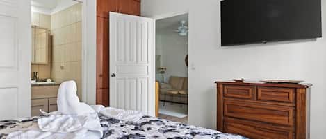 Un dormitorio con cama, cómoda de madera, televisor y baño visible a través de una puerta abierta.