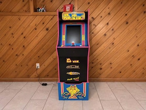 Una màquina recreativa de Pac-Man amb una combinació de colors rosa i blava, col·locada davant d'una paret de fusta.