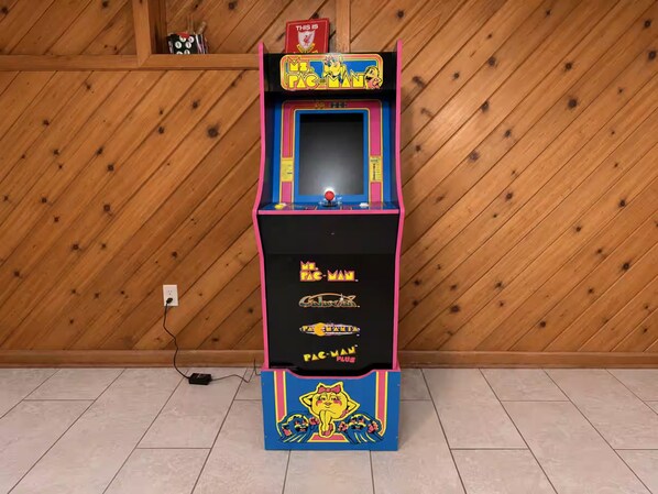 A Pac-Man arcade machine with a pink and blue color scheme, placed against a wooden wall.