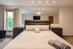 Un dormitorio moderno con una cama grande, dos mesitas de noche, una silla y un espejo amplio.