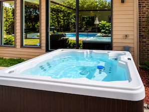 Un jacuzzi con vista a una piscina y una casa al fondo.