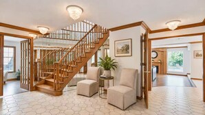 Amplia sala de estar con una escalera de madera, suelo con un patrón hexagonal y un ventanal grande.