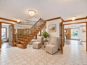 A spacious living area with a wooden staircase, hexagonal patterned flooring, and a large window.