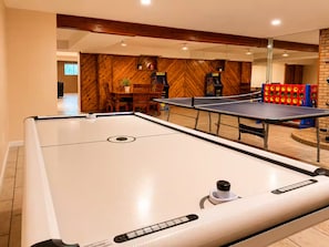 A pool table in a room with wooden walls and a dining area in the background.