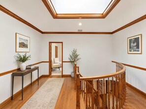 A hallway with a wooden staircase, a skylight, and two framed pictures on the walls.