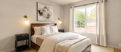 A bedroom with a bed, bedside tables, a ceiling fan, a window with curtains, and a wall-mounted artwork.