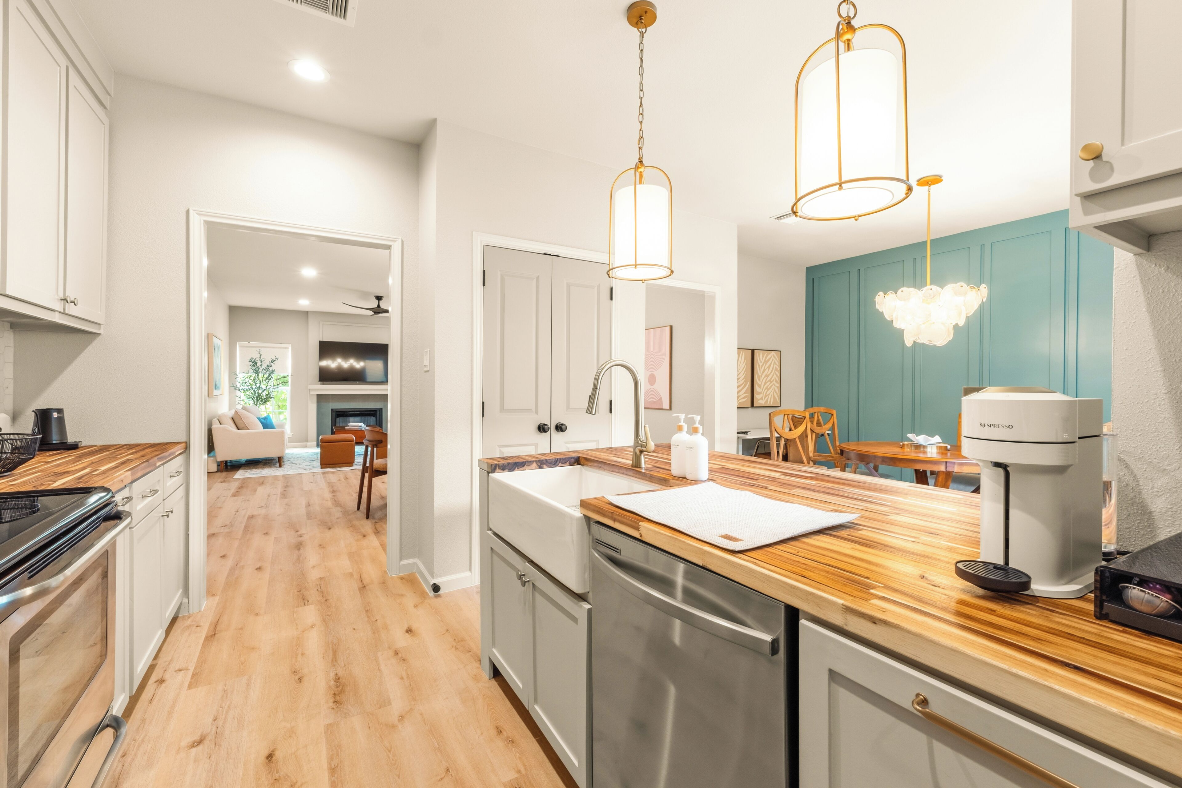 Cocina moderna con encimera de madera, electrodomésticos de acero inoxidable e iluminación colgante.