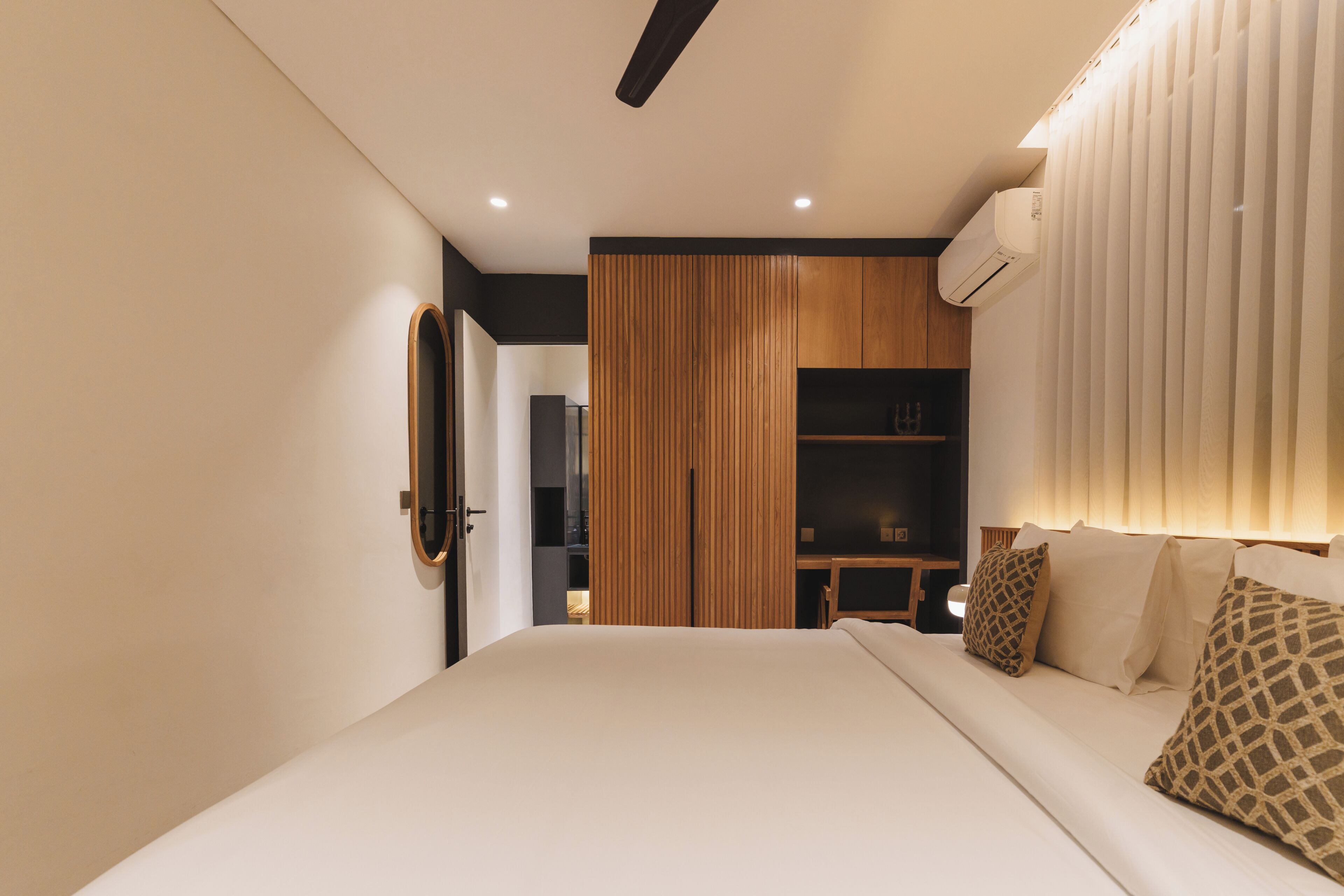 A modern bedroom with a bed, a wooden wardrobe, a desk, and a large window with blinds.