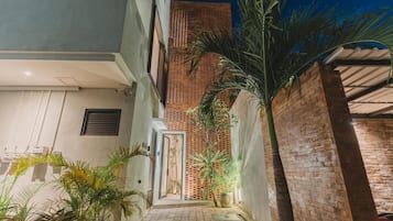 Un estrecho callejón con pared de ladrillo, puerta de metal y plantas en macetas.