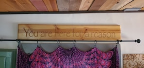 A wooden sign with the text 'You are here for a reason' mounted above a rack with patterned fabric items.