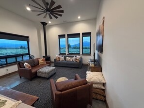 A living room with a fireplace, large windows, and a view of the outdoors. - Peaceful 2-bedroom cabin in West Yellowstone for a relaxing stay. (West Yellowstone)