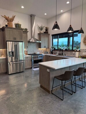 A modern kitchen with stainless steel appliances, wooden cabinets, and a large island with bar stools. - Peaceful 2-bedroom cabin in West Yellowstone for a relaxing stay. (West Yellowstone)