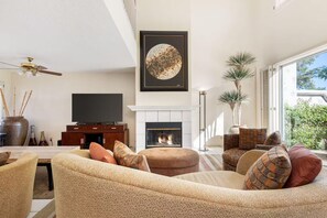 A living room with a fireplace, a television, and a large window. - 4BR Desert Retreat on the Golf Course Desert Falls (Palm Desert)