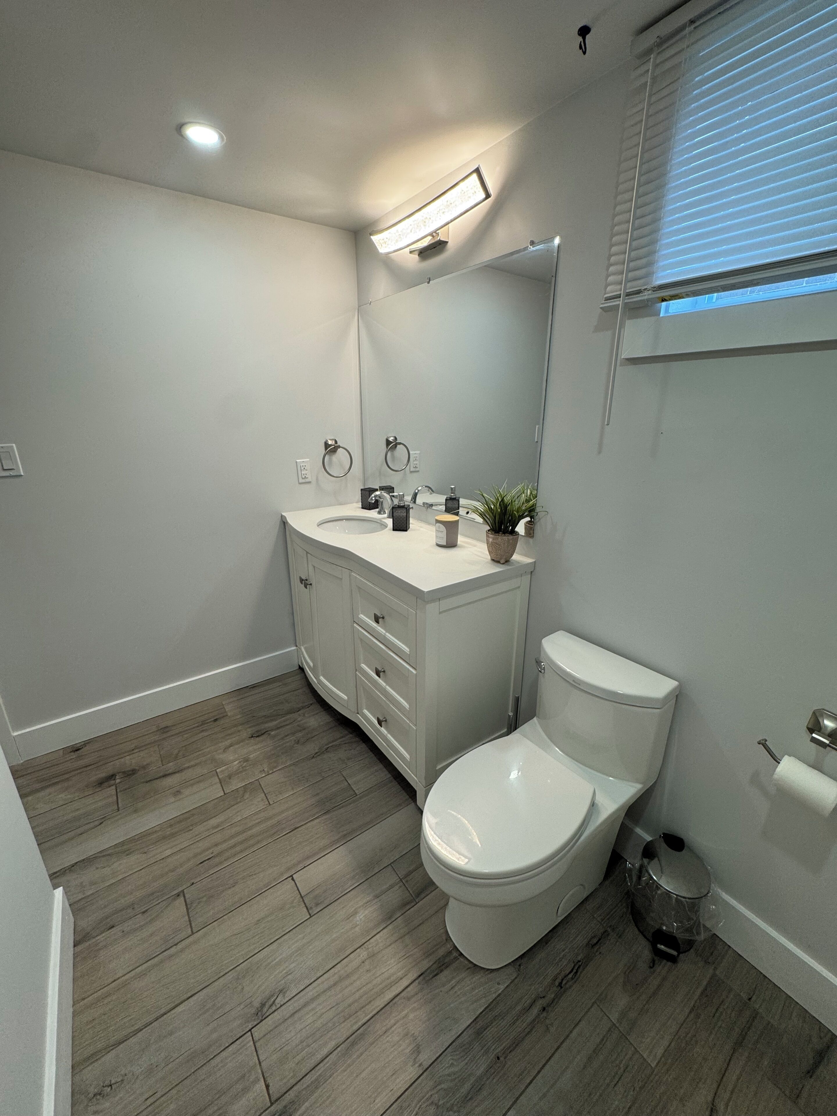A bathroom with a white vanity, a toilet, and a wooden floor.