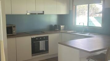 A compact kitchen with white cabinets, a microwave, a kettle, and a sink.